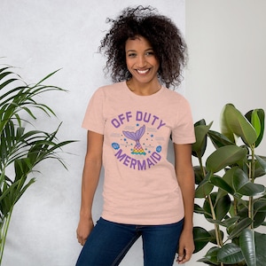 May include: A pink t-shirt with the text "Off Duty Mermaid" in a circle with a mermaid tail and other ocean-themed graphics.