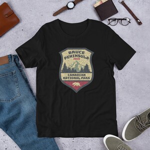 May include: Black t-shirt with a vintage-style graphic of a shield with the text "Bruce Peninsula 2019 Canadian National Park" and a bear silhouette.