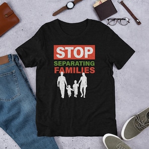 Puede incluir: Camiseta negra con un gráfico rojo y verde que dice "STOP SEPARATING FAMILIES". El gráfico también incluye una silueta de una familia de cuatro.