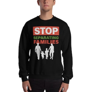 Puede incluir: Sudadera negra con un gráfico rojo y verde que dice "STOP SEPARATING FAMILIES" con una silueta de una familia tomada de la mano.