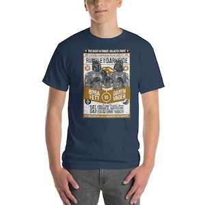 May include: A navy blue t-shirt with a vintage-style poster design featuring a boxing match between Boba Fett and Darth Vader. The poster reads "Rumble in Darkside" and includes the text "The Most Ultimate Galactic Fight".