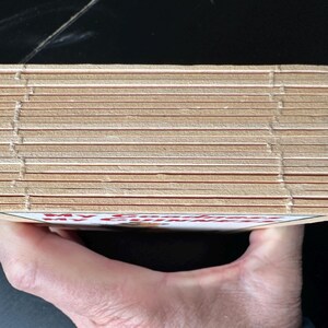 Puede incluir: Una pila de posavasos de color marr&oacute;n claro con bordes visibles y un dise&ntilde;o impreso en rojo y blanco. Los posavasos se sostienen en una mano, con el texto "MY COFFEE" visible.