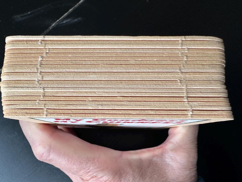 Puede incluir: Una pila de posavasos de color marr&oacute;n claro con bordes visibles y un dise&ntilde;o impreso en rojo y blanco. Los posavasos se sostienen en una mano, con el texto "MY COFFEE" visible.