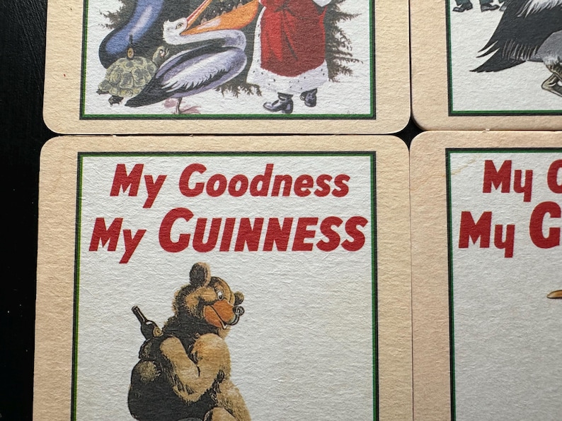Puede incluir: Posavasos cuadrados con borde crema y ribete verde. Los posavasos presentan ilustraciones de animales y Pap&aacute; Noel. Un posavasos tiene el texto "My Goodness My Guinness" en letras rojas.