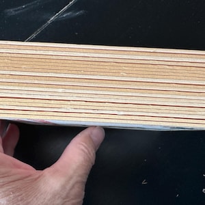 Puede incluir: Una pila de posavasos rectangulares de madera con esquinas redondeadas. Los posavasos son de color marr&oacute;n claro con una fina l&iacute;nea marr&oacute;n rojizo cerca de los bordes. La pila est&aacute; sostenida por una mano.