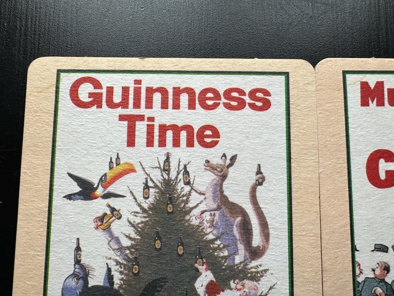 Puede incluir: Un posavasos vintage de Guinness Time con una ilustraci&oacute;n festiva. La imagen presenta un tuc&aacute;n, un canguro y otros animales alrededor de un &aacute;rbol de Navidad decorado con botellas de Guinness. El texto "Guinness Time" es rojo.