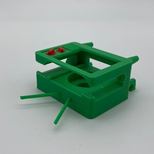Puede incluir: Soporte de c&aacute;mara impreso en 3D de pl&aacute;stico verde con dos botones rojos en la parte superior.