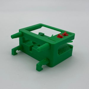 Puede incluir: Un modelo de televisi&oacute;n vintage de pl&aacute;stico verde con botones rojos. El modelo est&aacute; dise&ntilde;ado para ser utilizado como soporte para un objeto peque&ntilde;o.