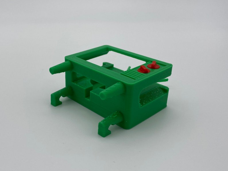 Puede incluir: Un modelo de televisi&oacute;n vintage de pl&aacute;stico verde con botones rojos. El modelo est&aacute; dise&ntilde;ado para ser utilizado como soporte para un objeto peque&ntilde;o.
