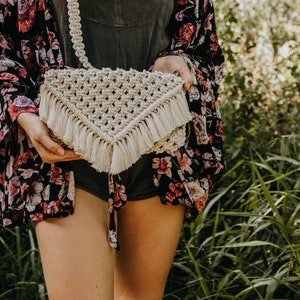 May include: A white crocheted bag with a fringe trim. The bag is worn as a crossbody bag.
