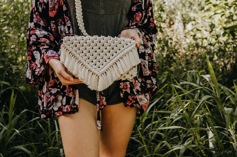 May include: A white crocheted bag with a fringe trim. The bag is worn as a crossbody bag.