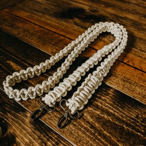 May include: Two white cotton camera straps with metal clasps. The straps are made of a thick, braided rope.