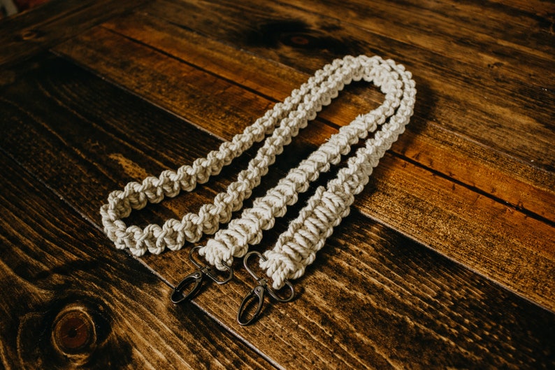 May include: Two white cotton camera straps with metal clasps. The straps are made of a thick, braided rope.