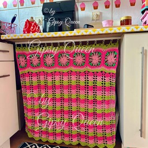 May include: A pink and green crocheted curtain with a scalloped bottom edge hangs from a white rod. The curtain is made of squares with flowers in the center. The text "by Gipsy Queen" is visible on the curtain.