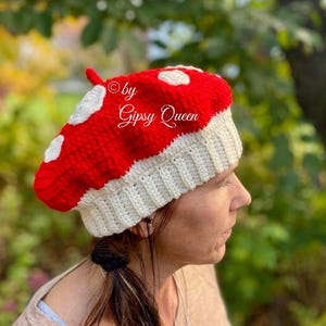 Puede incluir: Un gorro de punto rojo y blanco con forma de hongo con lunares blancos. El gorro tiene un borde de punto blanco y un pequeño pompón blanco en la parte superior. © by Gipsy Queen