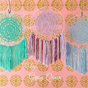 May include: Three handmade dream catchers in shades of teal, lavender, and blue. Each features a crocheted circular web within a white hoop, with hanging fringe and decorative tassels. The background is pink with a gold floral pattern. The text "by Gipsy Queen" is visible.