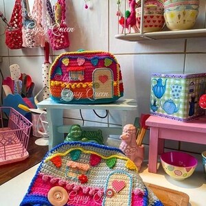May include: A colorful, crocheted camper-shaped item with a door, window, and decorative elements. The camper is primarily pink, blue, and yellow, with a large wooden button. The text "Gipsy Queen" is visible.
