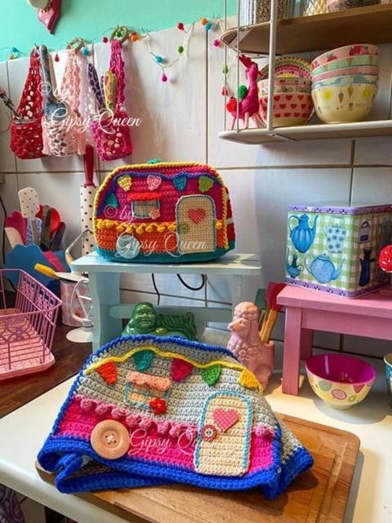 May include: A colorful, crocheted camper-shaped item with a door, window, and decorative elements. The camper is primarily pink, blue, and yellow, with a large wooden button. The text "Gipsy Queen" is visible.