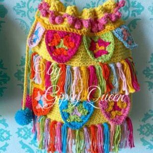 May include: A yellow crocheted bag with colorful tassels and a variety of crocheted flowers. The bag has a long strap and is decorated with pom-poms.