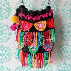 May include: A black crocheted bag with colorful tassels and floral designs. The bag has a long strap and is decorated with pom-poms.