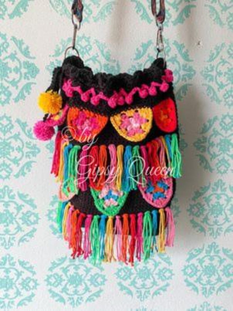 May include: A black crocheted bag with colorful tassels and floral designs. The bag has a long strap and is decorated with pom-poms.