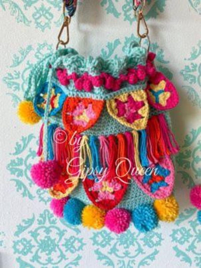 May include: A crocheted turquoise bag with colorful pom-poms and fringe. The bag has a variety of colorful crocheted designs and the text "by Gipsy Queen" is visible.