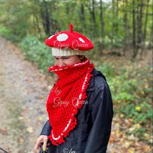 May include: A red and white crocheted mushroom hat with white polka dots. The hat is worn by a person in a black jacket. The text "by Gipsy Queen" is visible on the hat.
