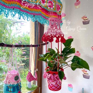 May include: Three crocheted plant hangers in pink, blue, and green, hanging from a branch. The hangers are decorated with flowers and other details. The plant hangers are labeled "by Gipsy Queen".