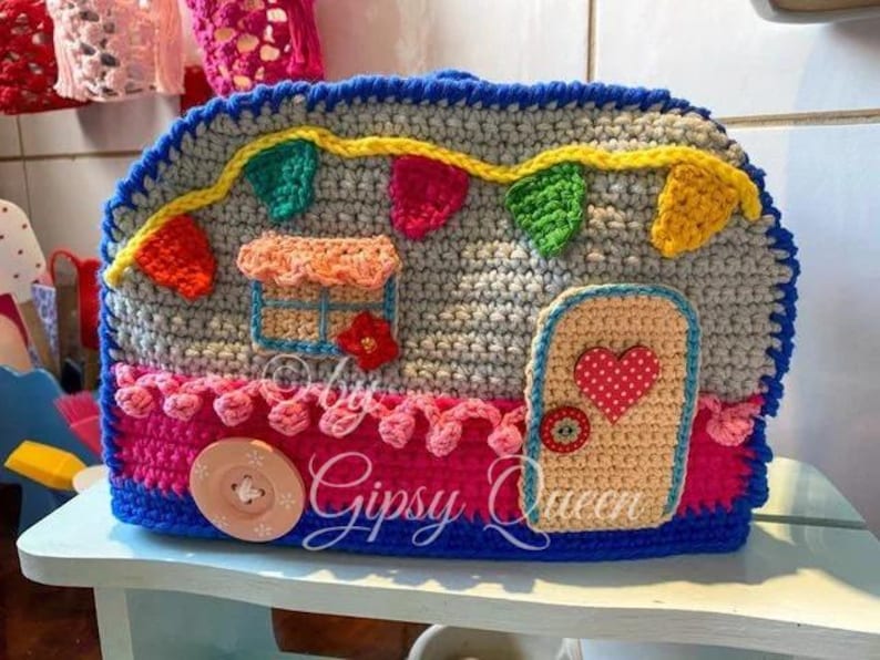 May include: A handmade crochet camper with a gray body, blue trim, and colorful accents. Features a door with a heart, a window, and decorative bunting. The text "Gipsy Queen" is visible.