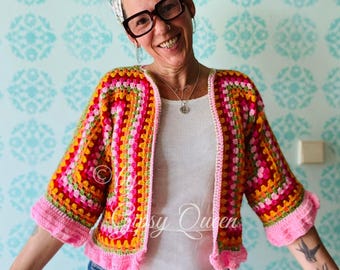 May include: A colorful crocheted cardigan with a pink, orange, yellow, green, and red striped pattern. The cardigan has a white background and a ruffled hem. The model is wearing blue jeans and a white shirt.