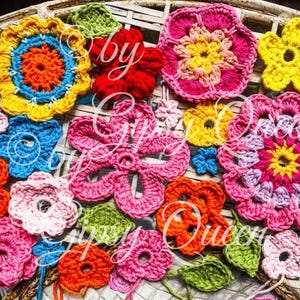 May include: A collection of crocheted flower shapes in various colors, including pink, yellow, orange, red, and blue. The flowers are arranged on a woven surface.