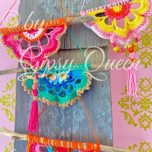 Pode incluir: Tr&ecirc;s tape&ccedil;arias de parede de croch&ecirc; coloridas com franjas, cada uma pendurada em um galho em um fundo de madeira. As tape&ccedil;arias s&atilde;o em tons de rosa, amarelo, laranja, verde e azul.