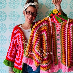 Op de afbeelding: Twee kleurrijke gehaakte vesten met een kleurenschema van roze, rood, groen, geel en oranje. De vesten hebben een gehaakt bloemenontwerp op de kraag en een gegolfde zoom.