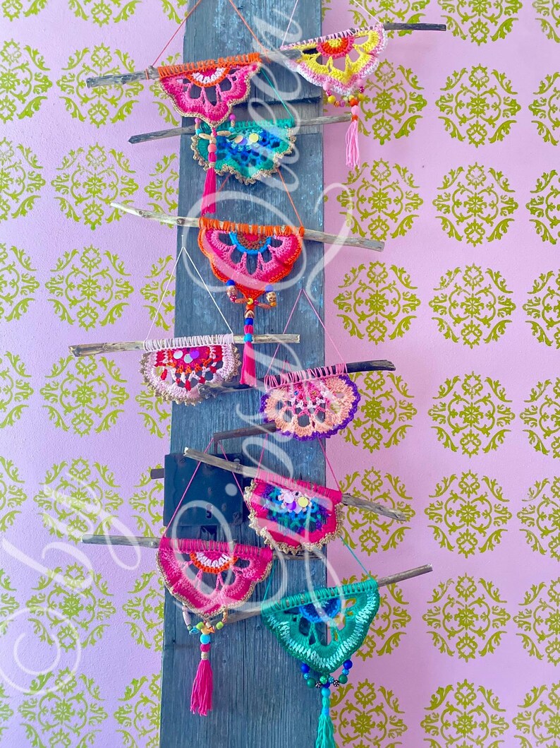 Pode incluir: Uma cole&ccedil;&atilde;o de tape&ccedil;arias de parede de croch&ecirc; coloridas com borlas de contas, exibidas em uma parede de madeira. As tape&ccedil;arias s&atilde;o de v&aacute;rias formas e tamanhos, com uma mistura de cores rosa, verde, azul, laranja e amarelo.