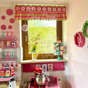 May include: A pink and green crocheted window valance with a scalloped edge. The valance is decorated with pink and white flowers. The valance is hanging in a kitchen window with a pink and white polka dot wall behind it. The text "Gipsy Queen" is visible in the image.