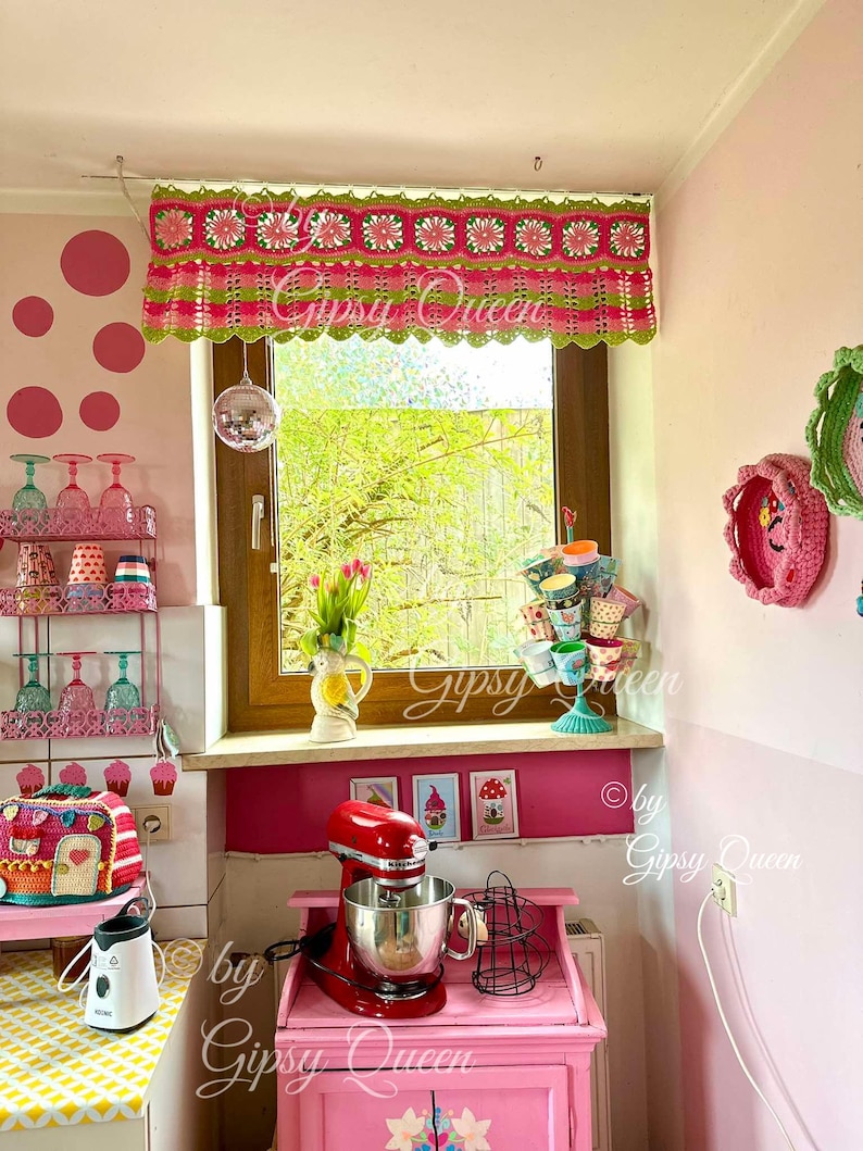 May include: A pink and green crocheted window valance with a scalloped edge. The valance is decorated with pink and white flowers. The valance is hanging in a kitchen window with a pink and white polka dot wall behind it. The text "Gipsy Queen" is visible in the image.