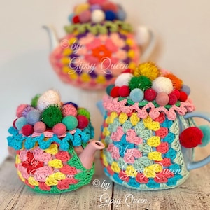 Könnte beinhalten: Drei bunte Häkel-Teekannenbezüge mit Bommeln. Die Bezüge sind in den Farben Rosa, Blau, Grün und Gelb gehalten. Der Text "by Gipsy Queen" ist auf den Bezügen sichtbar.