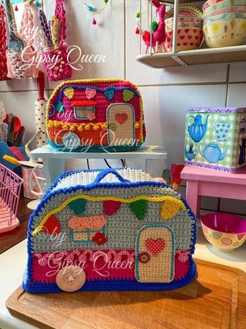 May include: Two colorful crochet camper-shaped bags. The top bag is red, orange, and blue, with a door and heart detail. The bottom bag is gray, blue, and pink, with a door and heart detail. The text "by Gipsy Queen" is visible.
