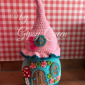 May include: A crocheted gnome house with a pink roof, blue and green details, and a mushroom door. The house is decorated with flowers and a window. The text "by Gipsy Queen" is visible on the image.