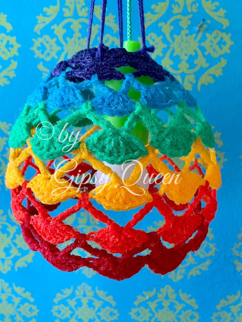 May include: A rainbow crocheted lampshade with a white lightbulb inside. The lampshade is hanging from a ceiling and is made of different colored yarn.