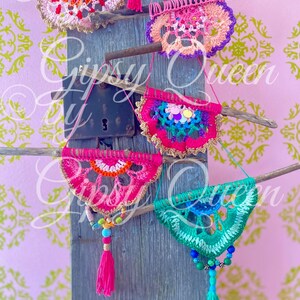 Pode incluir: Cinco tape&ccedil;arias de parede de croch&ecirc; em v&aacute;rias cores, incluindo rosa, verde, azul e laranja, s&atilde;o exibidas em uma superf&iacute;cie de madeira. Cada tape&ccedil;aria apresenta um design circular com uma franja de contas.