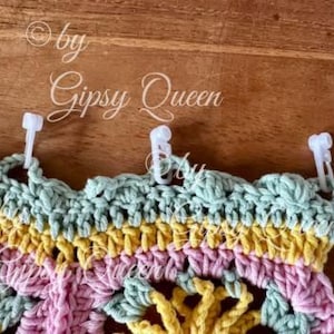 May include: A multi-colored crocheted piece with a scalloped edge. The piece is attached to a wooden surface with white plastic clips.