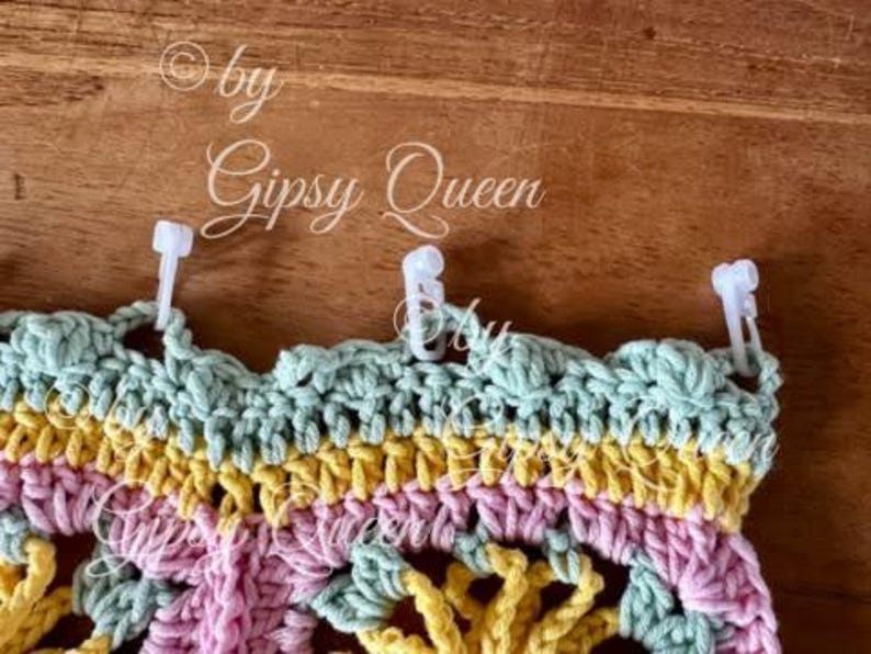 May include: A multi-colored crocheted piece with a scalloped edge. The piece is attached to a wooden surface with white plastic clips.