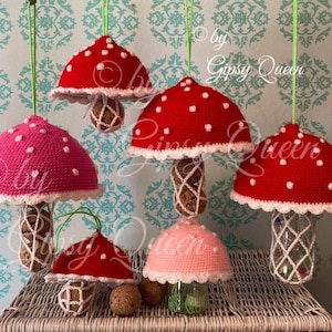 May include: Six crocheted mushroom ornaments with white polka dots and white trim. The mushrooms are hanging from the ceiling and have a white crocheted base. The mushrooms are red and pink.
