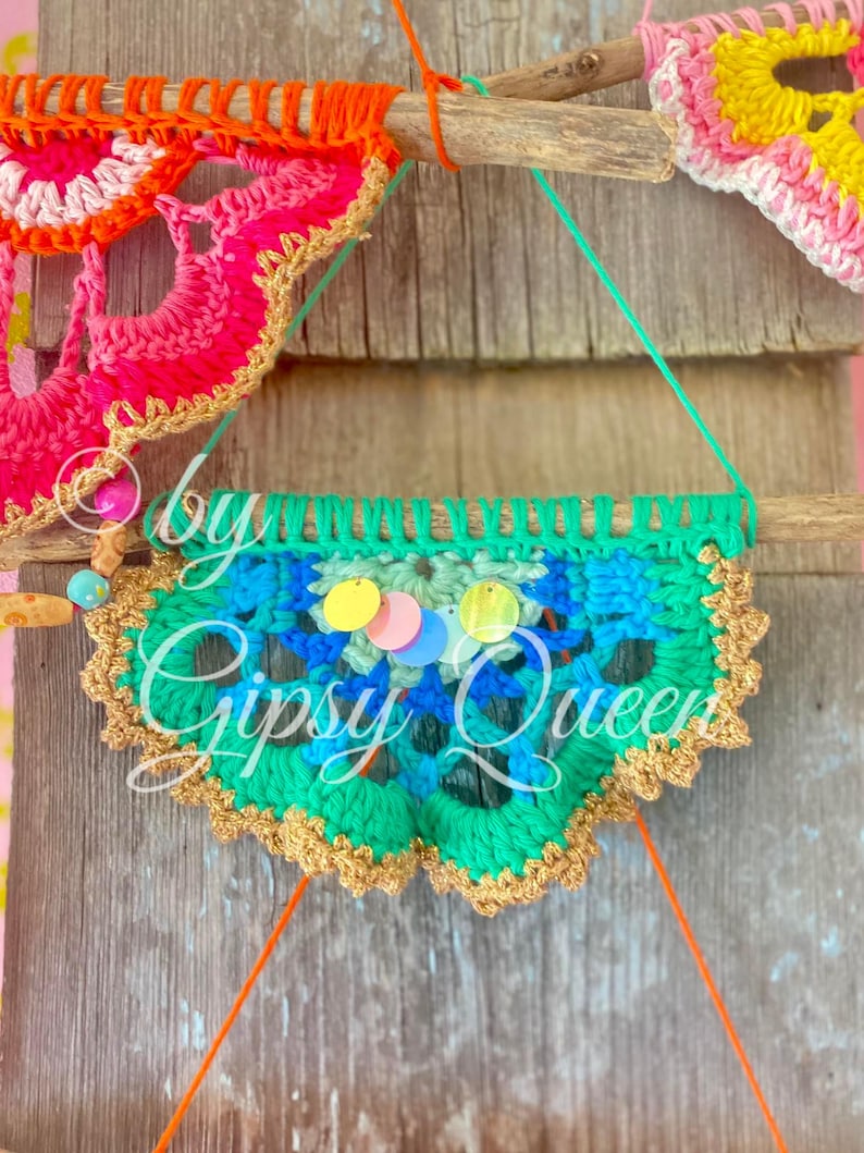 Pode incluir: Uma faixa de croch&ecirc; verde, azul e dourado com lantejoulas coloridas penduradas em um galho. A faixa tem o texto "Gipsy Queen".