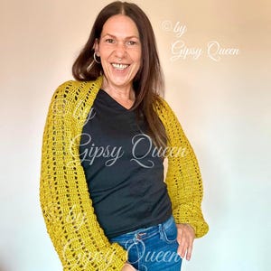 Könnte beinhalten: Ein senfgelber Häkelcardigan mit langen Ärmeln und lockerer Passform. Der Cardigan wird über einem schwarzen T-Shirt und einer blauen Jeans getragen. Der Text "by Gipsy Queen" ist in der oberen rechten Ecke des Bildes sichtbar.