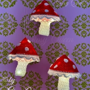 May include: Three hanging crochet mushroom ornaments featuring red caps with white spots and white stems. Each mushroom has a scalloped white edge around the base of the cap. The text "By Gipsy Queen" is visible in the background.