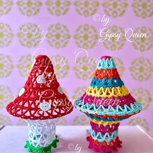 Può includere: Due lampade a forma di fungo all'uncinetto. Una è rossa con pois bianchi, l'altra è multicolore con blu, giallo, arancione e rosa. Le lampade hanno una base bianca e rifiniture verdi. Lo sfondo è rosa a fantasia.