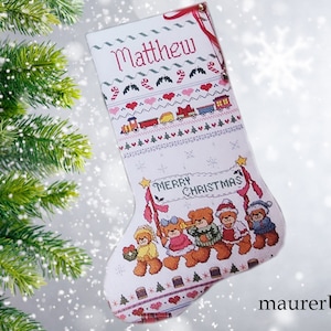 May include: White Christmas stocking with a red and white candy cane border, a train design, and a group of teddy bears holding a banner that says "Merry Christmas". The stocking is personalized with the name "Matthew".