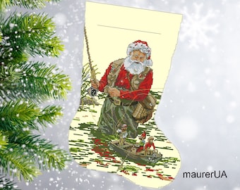 Op de afbeelding: Een kerstsok met een witte achtergrond toont een kerstman gekleed in rood en groen die aan het vissen is in een rivier. Hij houdt een hengel vast en er zijn twee kleinere figuren in een boot in het water. De sok heeft de tekst "maurerUA" onderaan.